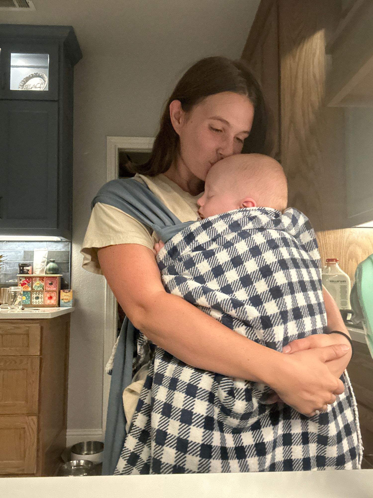 Tally kissing the head of her sleeping baby, wrapped against her chest in a carrier
